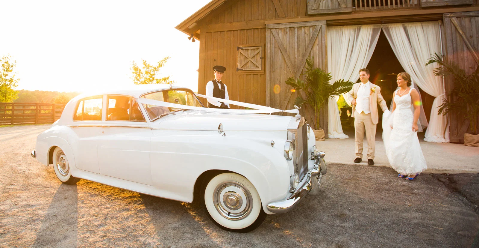 A white classic Rolls-Royce and newlyweds at a decorated rustic wedding venue